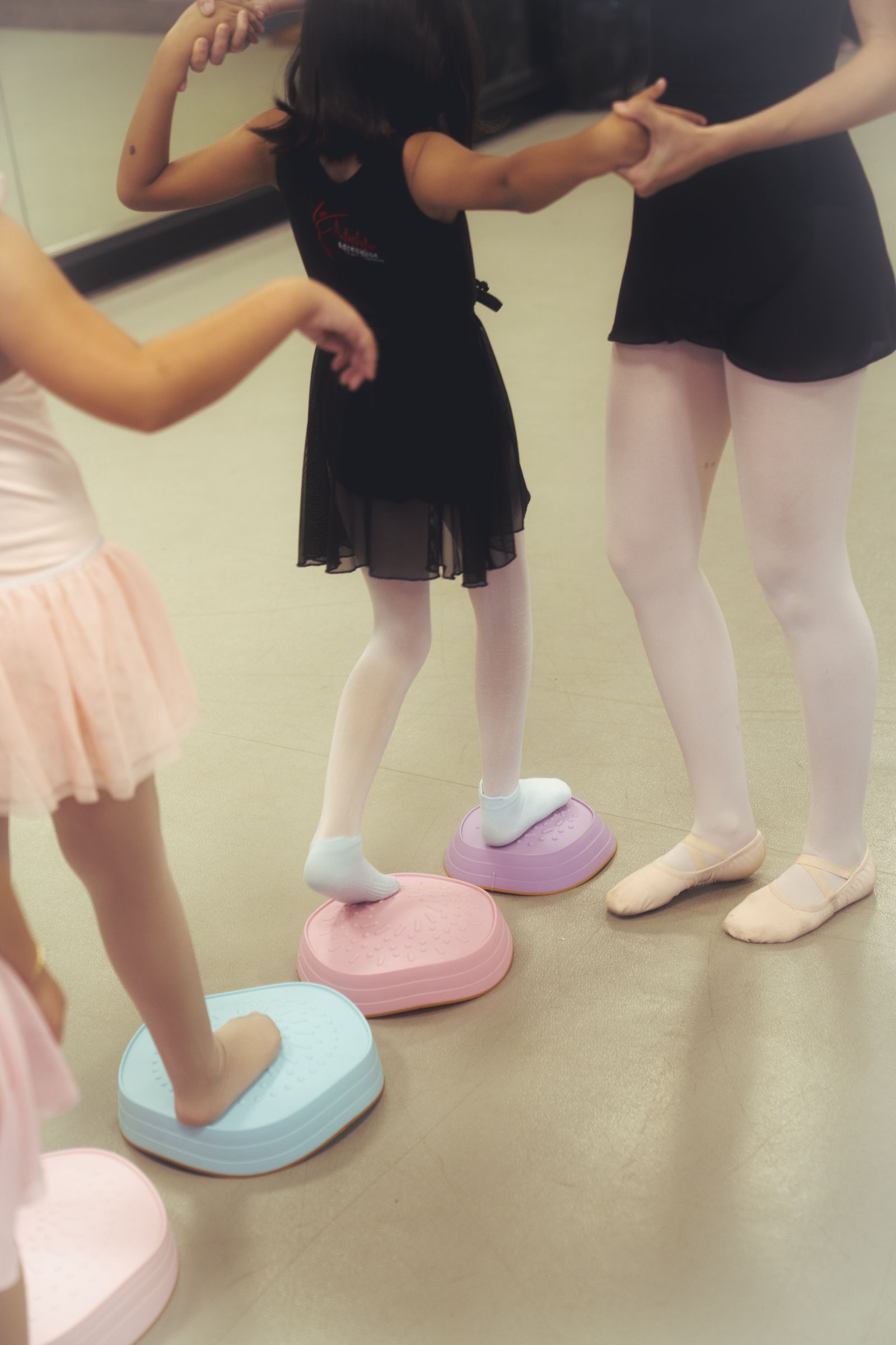 Young dancers step across colorful balance stones with an instructor alongside.