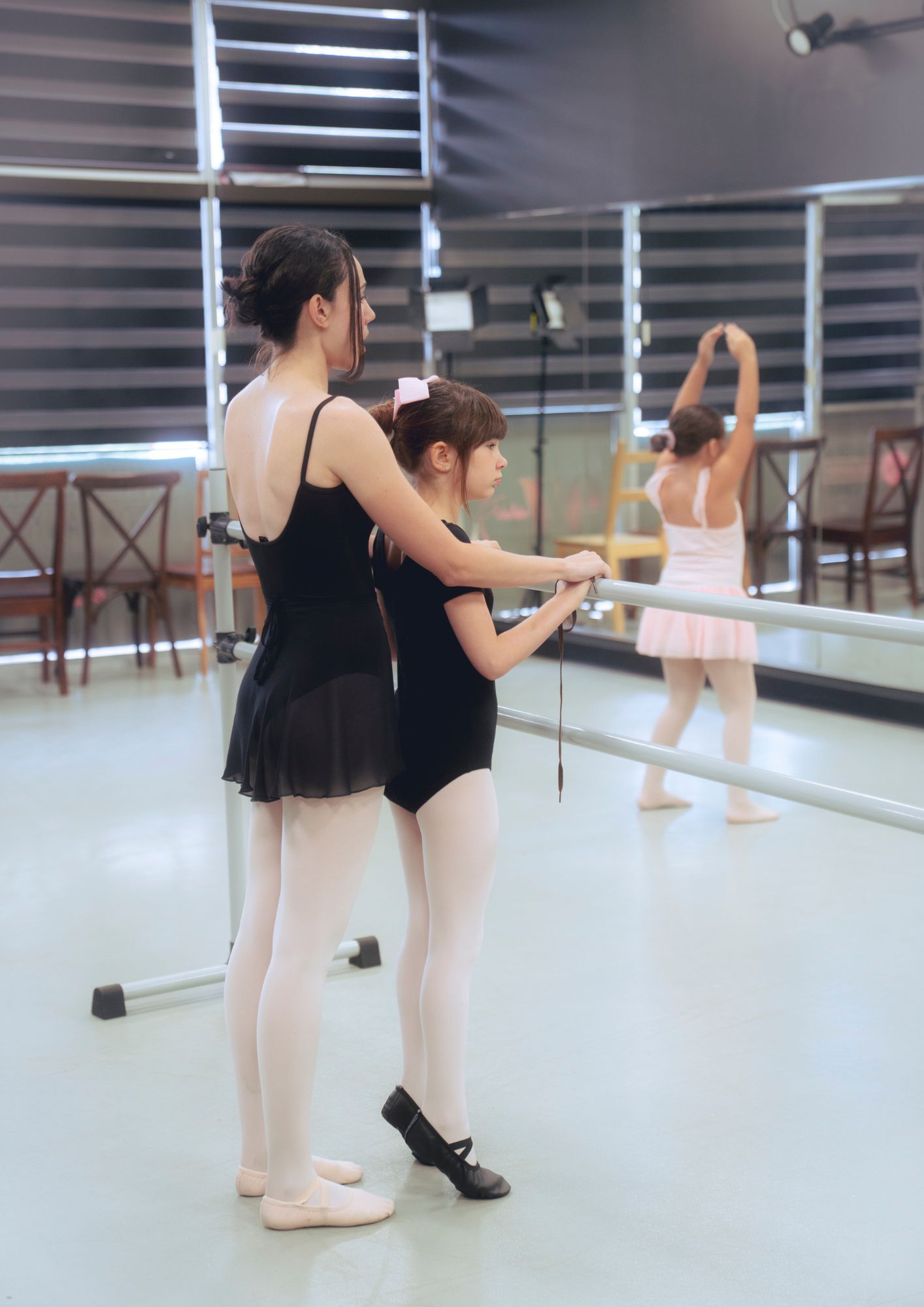 An instructor guides a young dancer at the barre.