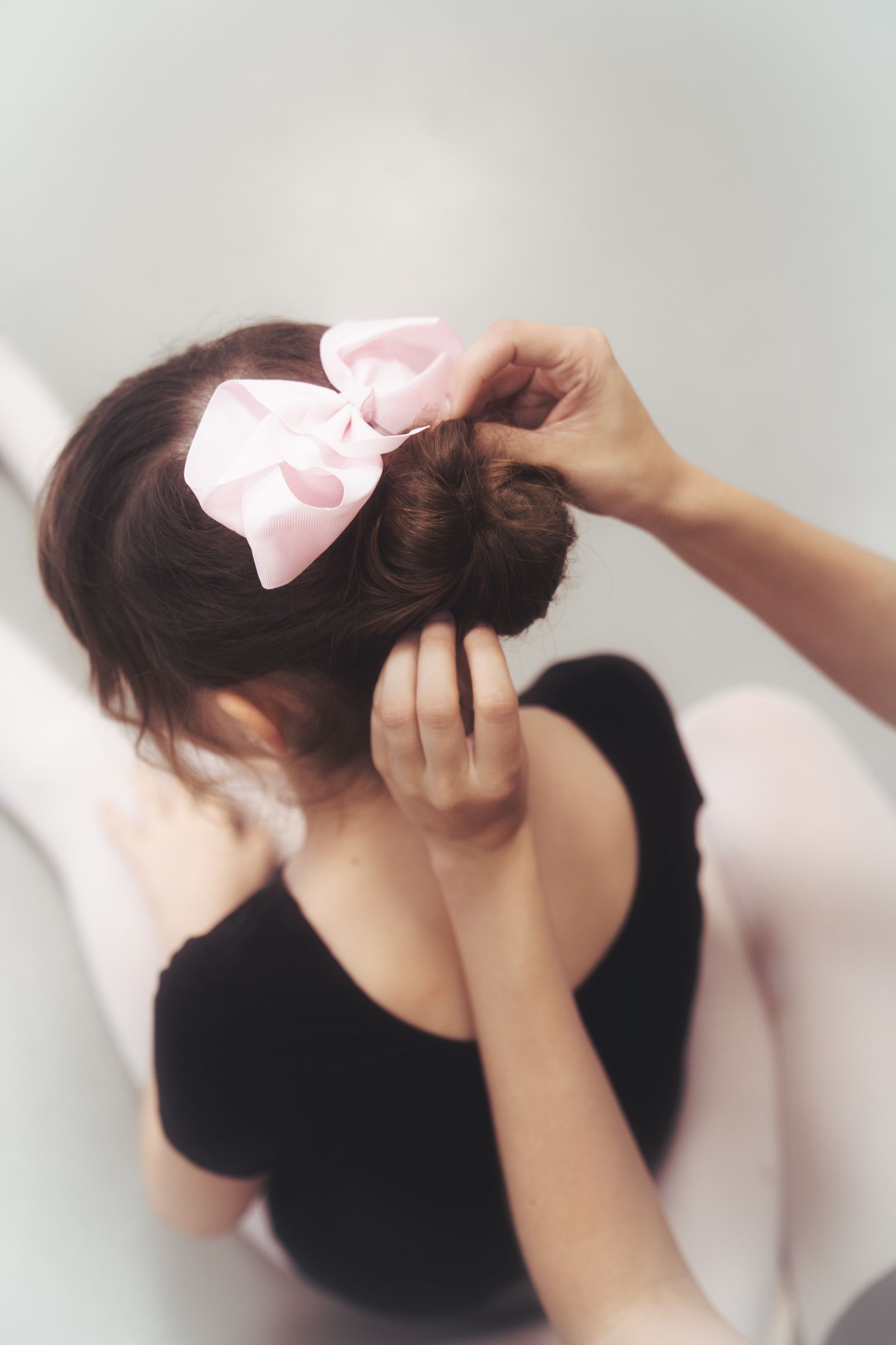 Hands securing a dancer's bun and pink bow before class begins.
